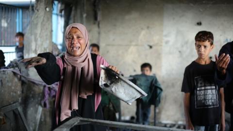 A woman cries with an outstretched hand as residents inspect the damage after Israeli attacks on Ard al-Mufti School 