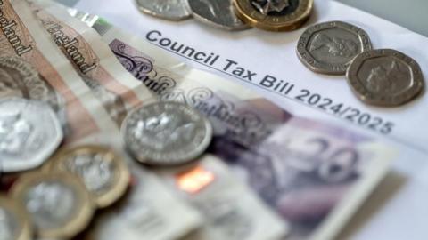Money in the form of coins and notes stacked on top of a council tax bill dated 2024-25