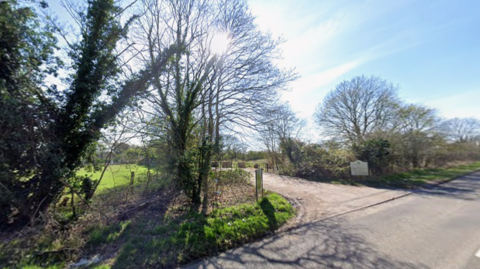 The entrance to a closed golf course, showing a driveway surrounded by trees.