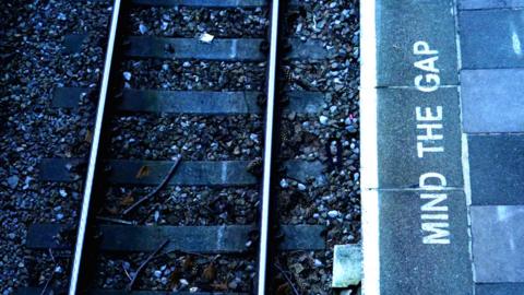 A railway track with the platform on the right and the words Mind The Gap