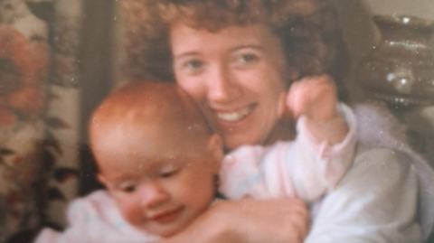 Young woman with red curly hair, smiling and holding a baby