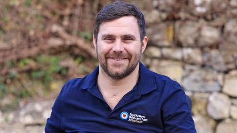 A smiling bearded man in a blue 'Royal Air Force Benevolent Fund' polo shirt