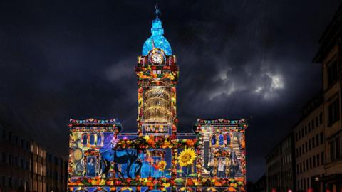 Market Hall in Chesterfield illuminated by colourful artwork which includes a sunflower, horse, and other colourful details.