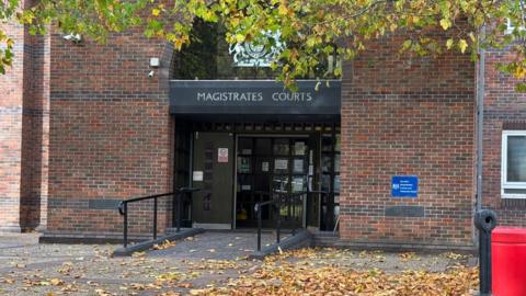 A view of the entrance of red brick building. A ramp leads up to a set of double doors. A sign above says "Magistrates Court".
