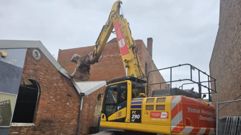 Orange brick building with yellow tractor infront 