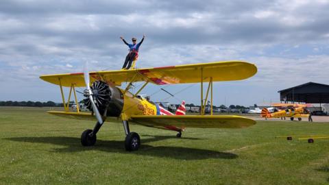 An elderly woman is strapped onto the yellow wings of a plane. 