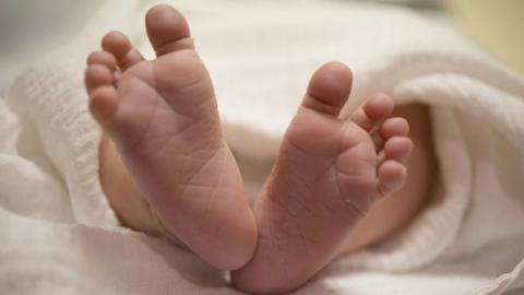 Image of a newborn baby's feet. All toes are visible. The baby is wrapped in a white blanket 