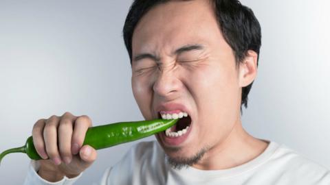 A man in pain biting a large green chilli