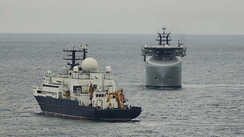 Russian ship Yantar in the  foreground being watched by a Royal Navy ship close by 