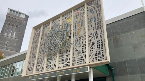 The front of the Plymouth Crown Court building on a grey day. A sign reads CROWN AND COUNTY COURTS and above it is an elaborately designed set of windows.