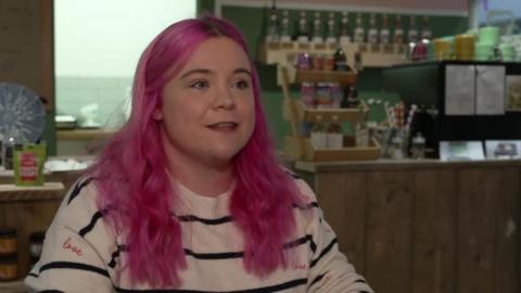 A woman with long pink hair wearing a white and black striped jumper.
