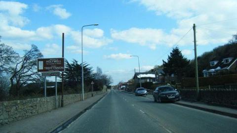 Photo of Ffordd Holway in Holywell in Flintshire. Cars are visible parked on the curb and there's a sign for Holywell/ Treffynnon on the left. There are houses on the right hand side. 