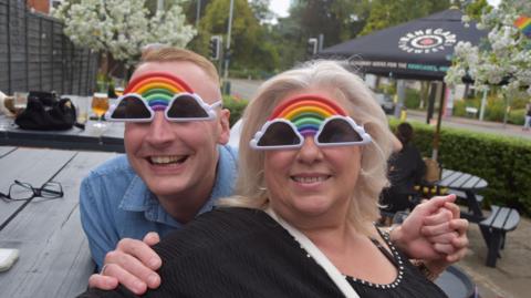 Two people with rainbow sunglasses outside a pub