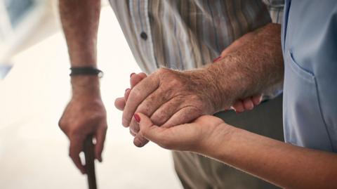 Female nurse supporting senior man to walk. Focus on hands.