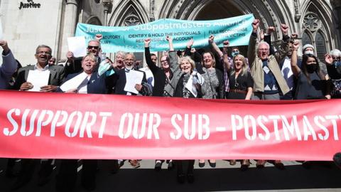 Former post office workers celebrate with raised fists and a large red banner that says 'support our sub-postmasters' outside the Royal Courts of Justice, London, after having their convictions overturned by the Court of Appeal in April 2021