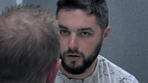 A still of the episode of 24 Hours in Police Custody where Adam White, with short hair and a beard, is looking concerned during a police interview