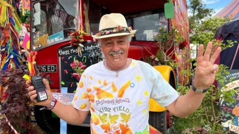 A man in a white t shirt and sun hat standing in front of a red double decker bus.