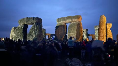 A crowd of people gather at Stonehenge, which has been illuminated to mark winter solstice 