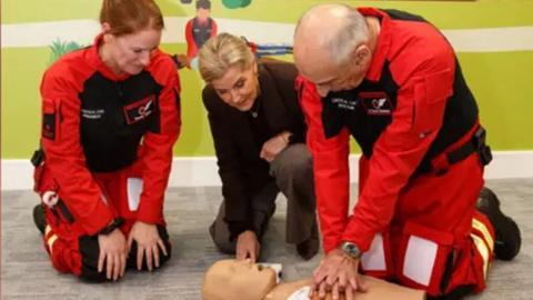 The Duchess of Edinburgh along with two Air Ambulance members perform CPR on a manikin. 