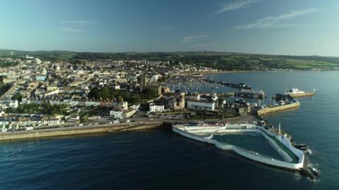 An aerial view of Penzance, Cornwall, on a sunny day - showing the town, the coastline, and Jubilee Pool