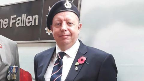 An image of Andrew Johnson showing his head, shoulders and chest as he stands looking at the camera wearing a suit and tie with beret and poppy on his lapel
