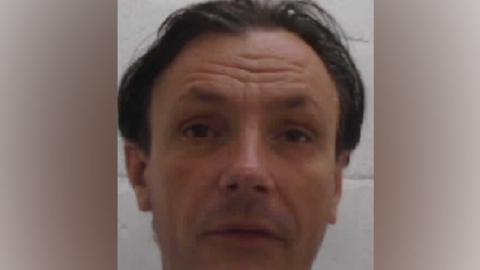 A Marcus Yeldham mugshot that is fairly blurry. He has dark, ear-length hair parted in the middle and has both his eyebrows raised