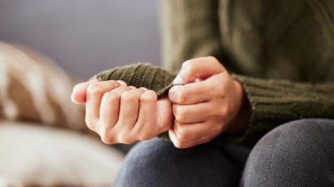 A woman in a green cardigan pulls at her sleeve