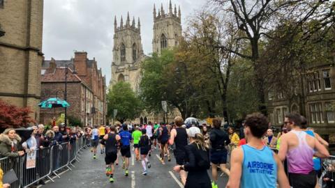 Runners race towards York Minster while crowds in coats and umbrellas watch on at the side 
