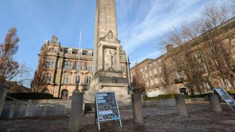 Two A-boards saying 'Respect this space' are placed in front of the stone columns and chains that surround the Cenotaph in Preston. 