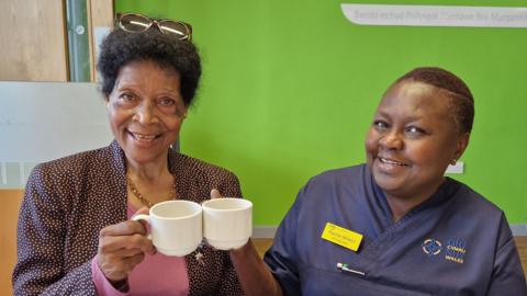 Agnes Musikavanhu and Rachel Wilson, they are both smiling and looking at the camera, and cheersing a cup of tea