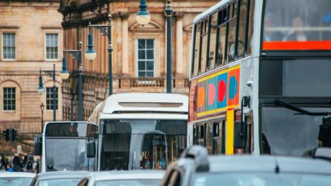 A close up picture of a queue of cars and buses on a street in Edinburgh driving towards the camera. 