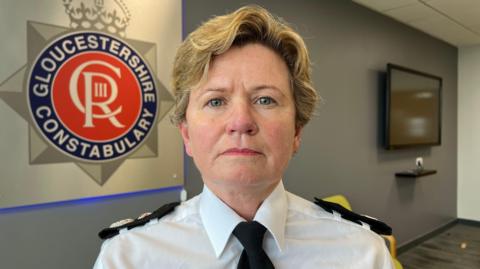 Head and shoulders shot of Temporary Chief Constable Maggie Blyth. She has short blonde hair and is wearing a police uniform. She is standing in front of a Gloucestershire Constabulary logo.