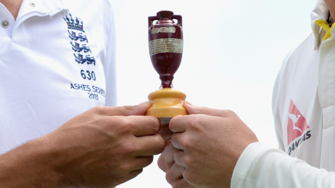 An England and Australia player holding the Ashes urn between them