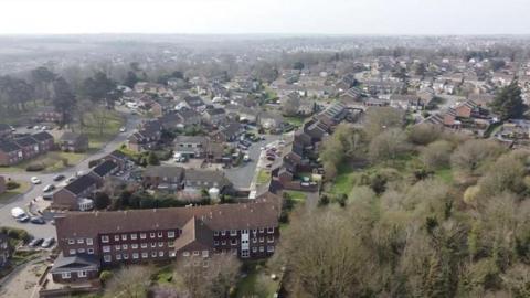 A drone image over part of a residential area of a town. Homes, blocks of flats and trees can be seen. 