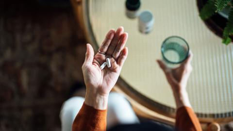 Close up of a person's hand holding two white pills, with a glass of water in their other hand