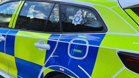 The side of a police car with yellow and blue square livery and a Humberside Police force logo on the rear passenger window.