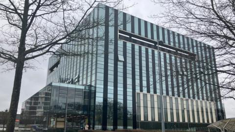A glass building in a cube design in the middle of a town square.