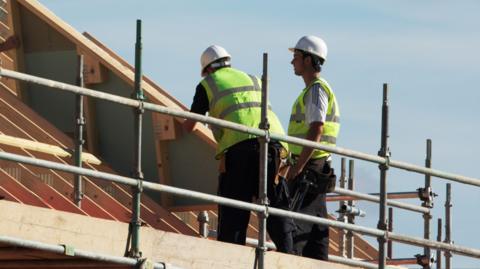 Two builders standing on a scaffolding working on a roof