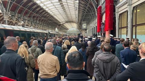 A crowd of people fill a platform at London Paddington Station to mark Armistice Day