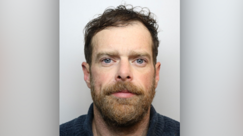 A man with a beard and blue jumper looking at the camera.