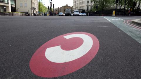 Congestion charge zone marking - a white 'c' on a red circle painted on a road in London 