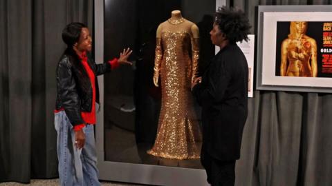 Angellica Bell looks at a gold dress with another woman.