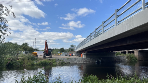 A bridge over the River Roar with construction vehicles an the far bank