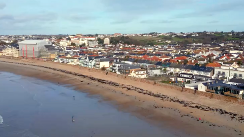 This is an aerial view of a beach with a seawall and houses directly behind it.