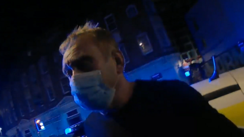A man wearing a face mask being arrested.