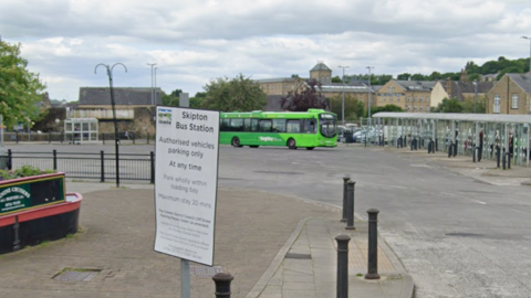 General view of Skipton Bus Station, with bollards and a green single-decker bus in the background.