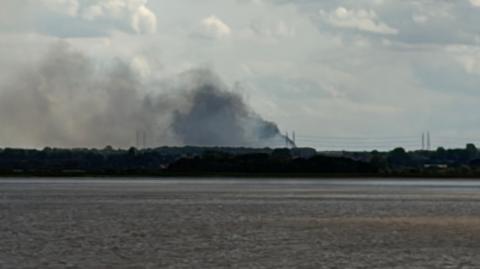 Plumes of smoke rise into the sky. There is a field in the foreground.