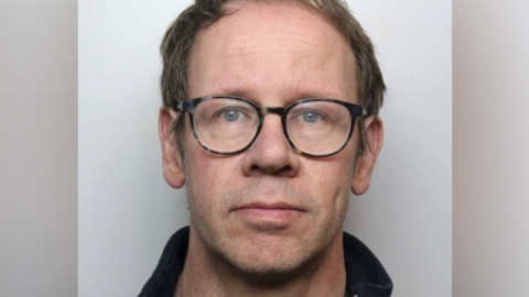A police mugshot of Matthew Isles. He is wearing glasses and is standing against a pale background.