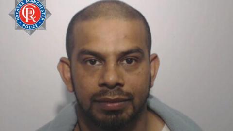 A police mugshot of Faruquz Zaman. He has closely shaven dark hair and a beard and is wearing a white T-shirt with either a grey fleece jacket or blanket over his shoulders. Part of the Greater Manchester Police logo can be seen in the top left hand corner.