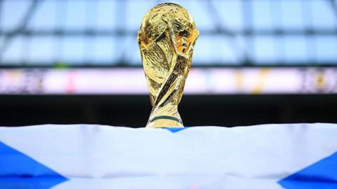 A World Cup trophy is perched on top of a Scotland flag.
